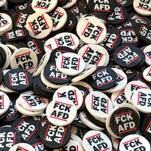 Könnte beinhalten: Ein Nahaufnahmebild eines Stapels runder schwarzer und weißer Knöpfe mit dem aufgedruckten Text "FCK AFD".