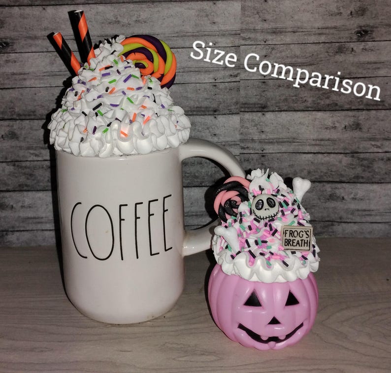 Puede incluir: Comparaci&oacute;n de tama&ntilde;o de dos tazas de caf&eacute; con tem&aacute;tica de Halloween. La taza m&aacute;s grande es blanca con la palabra "COFFEE" impresa en ella. Est&aacute; cubierta con crema batida blanca, chispas y un bast&oacute;n de caramelo. La taza m&aacute;s peque&ntilde;a es una calabaza rosa con una cara de Jack Skellington y un letrero de "FROGS BREATH". Tambi&eacute;n est&aacute; cubierta con crema batida, chispas y un bast&oacute;n de caramelo.