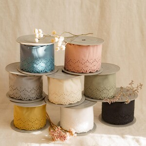Puede incluir: Una colección de carretes de cinta decorativa en varios colores, incluyendo azul, rosa, gris, crema, verde, amarillo, blanco y negro. Cada carrete presenta un diseño de borde festoneado. Flores secas dispuestas alrededor.