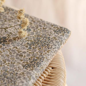 K&ouml;nnte beinhalten: Nahaufnahme eines Stoffes mit floralem Muster in Beige-, Gr&uuml;n- und Blaut&ouml;nen. Der Stoff ist &uuml;ber eine gewebte Korboberfl&auml;che drapiert. Getrocknete Blumen liegen auf dem Stoff und verleihen ihm eine nat&uuml;rliche Note.