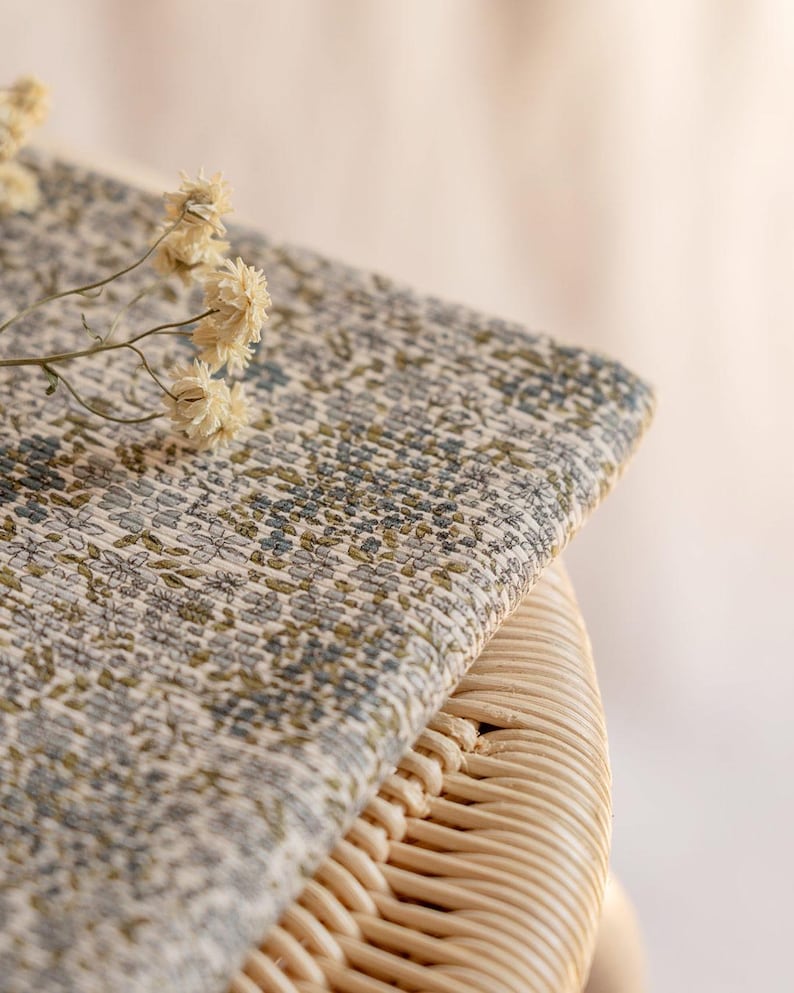 K&ouml;nnte beinhalten: Nahaufnahme eines Stoffes mit floralem Muster in Beige-, Gr&uuml;n- und Blaut&ouml;nen. Der Stoff ist &uuml;ber eine gewebte Korboberfl&auml;che drapiert. Getrocknete Blumen liegen auf dem Stoff und verleihen ihm eine nat&uuml;rliche Note.