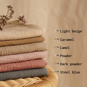 Op de afbeelding: Een stapel van zes stoffen stalen in verschillende kleuren, waaronder lichtbeige, karamel, camel, poeder, donker poeder en staalblauw. De stalen zijn voorzien van hun respectievelijke kleurnamen. De stof heeft een getextureerde, geribbelde uitstraling.