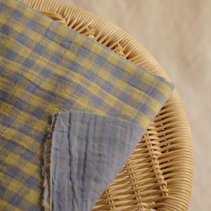 May include: A folded fabric with a blue and yellow checkered pattern, draped over a wicker chair. The fabric's reverse side is a solid blue. The image is well-lit, highlighting the texture and color of the textile.