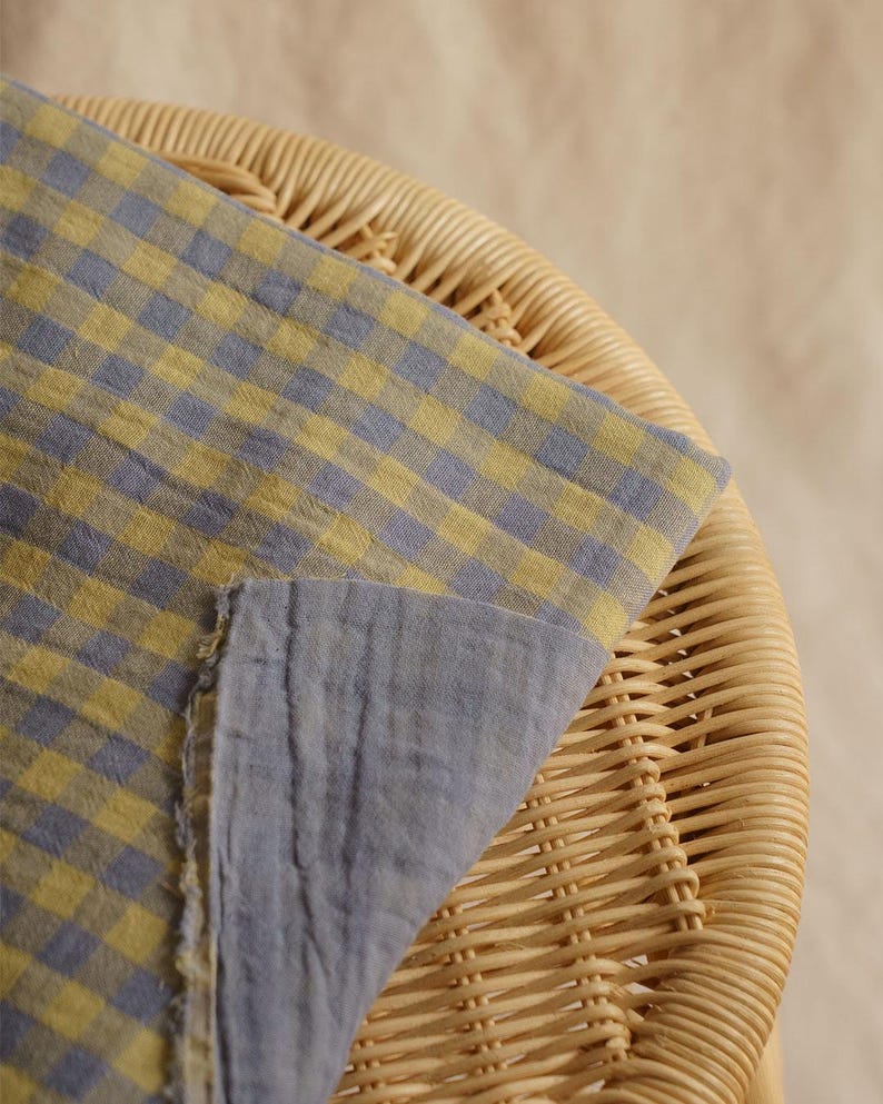 May include: A folded fabric with a blue and yellow checkered pattern, draped over a wicker chair. The fabric's reverse side is a solid blue. The image is well-lit, highlighting the texture and color of the textile.