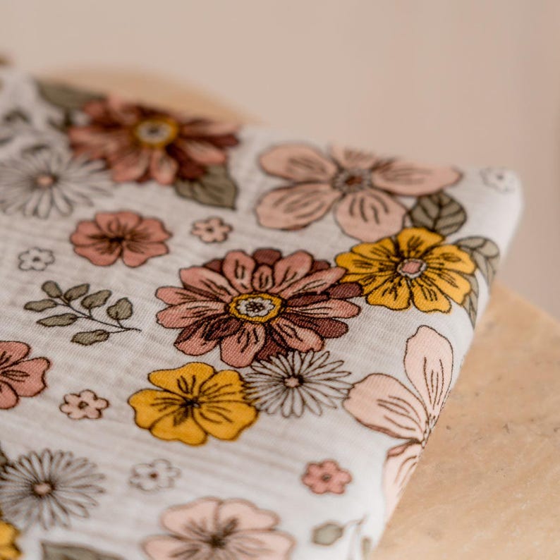 May include: White fabric with a floral print featuring pink, yellow, and brown flowers. The fabric has a soft, textured feel.