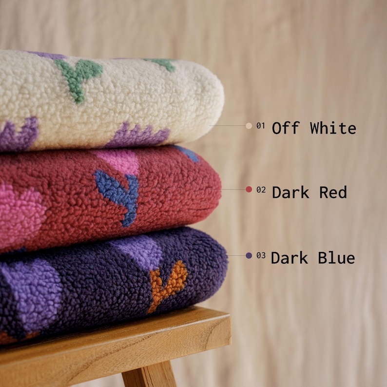 May include: Three stacked, textured fabric rolls in off-white, dark red, and dark blue. Each roll features a repeating floral pattern in contrasting colors. The image includes text labels: "Off White", "Dark Red", and "Dark Blue".