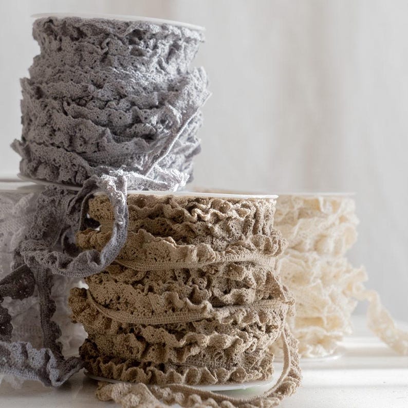 May include: Three spools of lace trim, one gray, one brown, and one white. The lace is ruffled and delicate.