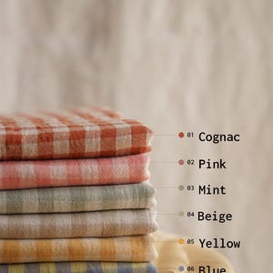 May include: A stack of six folded checkered fabric cloths in various colors: cognac, pink, mint, beige, yellow, and blue. Each cloth has a different color and is labeled with a number and color name.