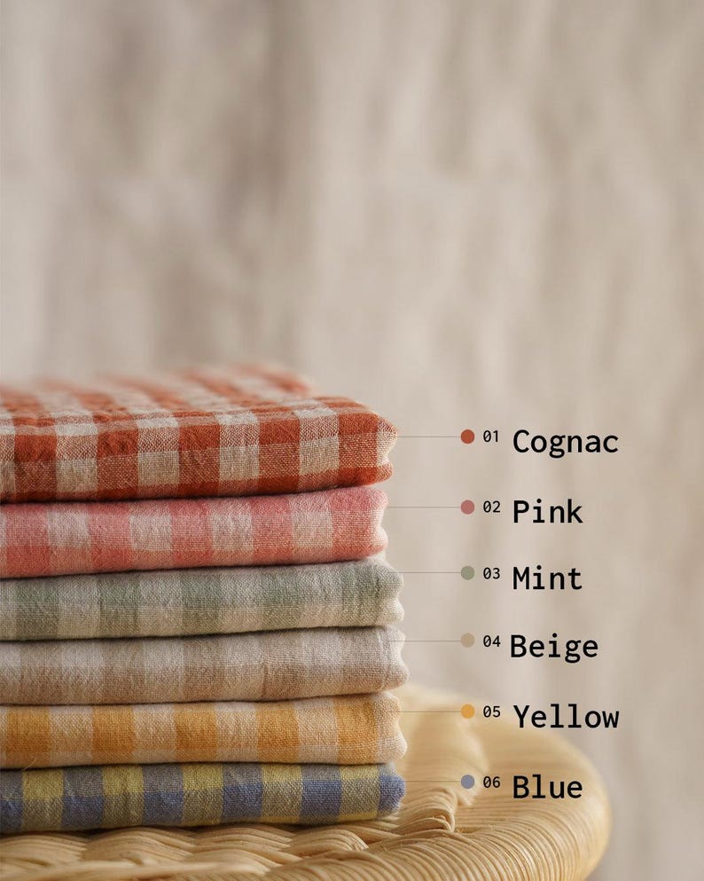 May include: A stack of six folded checkered fabric cloths in various colors: cognac, pink, mint, beige, yellow, and blue. Each cloth has a different color and is labeled with a number and color name.