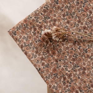 May include: A close-up of a beige fabric with a small-scale floral print in shades of brown and peach. The fabric is textured and has a subtle sheen.