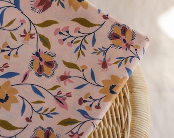 May include: A light pink fabric featuring a repeating floral pattern with stylized flowers and leaves in shades of mustard yellow, deep blue, olive green, and muted rose. The textile displays thin, dark stems connecting the various botanical elements.