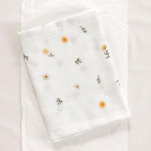 May include: White muslin baby blanket with embroidered yellow flowers and green stems.