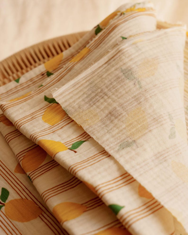 May include: Close-up of folded fabric with a lemon pattern. The fabric is off-white with brown stripes and yellow lemons with green leaves. The fabric is folded over a woven basket.