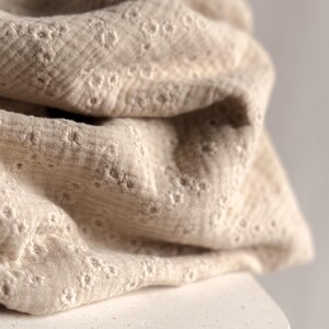 Op de afbeelding: Close-up van een beige stof met een delicaat, reli&euml;f bloemenpatroon. De stof is zacht en textuurrijk, met een subtiele glans.