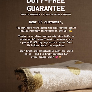 May include: A folded white and yellow patterned blanket rests on a wooden surface. The image includes text that reads "DUTY-FREE GUARANTEE" and a message to US customers about customs fees.