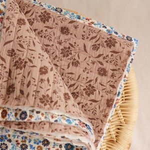 Peut inclure: Une pile de couvertures à motifs floraux dans les tons marron, bleu et crème. La couverture supérieure présente un motif floral marron sur un fond brun clair. Les bords des couvertures sont visibles, présentant divers motifs floraux.