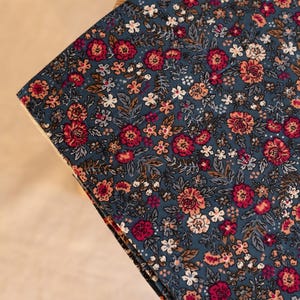 Könnte beinhalten: Ein gefaltetes Stück dunkelblauer Cordstoff mit einem dichten, sich wiederholenden Blumenmuster in den Farben Dunkelrot, zartes Rosa, Weiß und gedecktes Grün. Der Stoff weist die für Cord charakteristische vertikale Rippenstruktur auf.