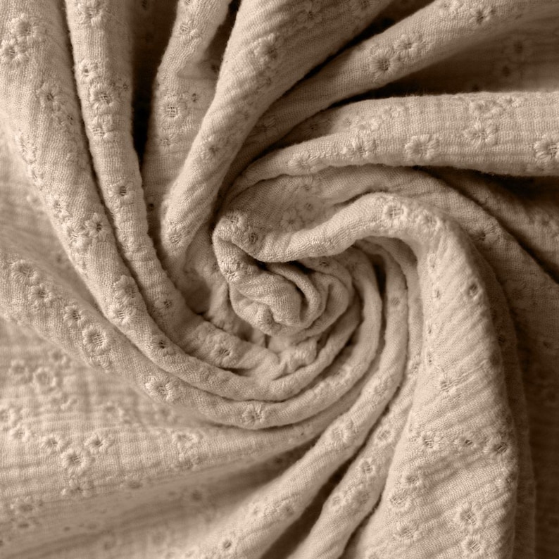 Op de afbeelding: Een close-up van een beige stof met een subtiel reli&euml;fpatroon. De stof is zacht en textuurrijk, met een licht gerimpelde uitstraling.