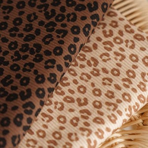 May include: Two fabrics with a leopard print design. One is dark brown with black spots, the other is light tan with brown spots. Both fabrics have a ribbed texture. Ideal for clothing or home decor.