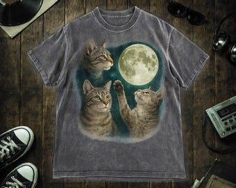 Pode incluir: Camiseta cinza escuro com um design extravagante de três gatos olhando para uma lua cheia. Os gatos são retratados em tons de cinza e marrom, com a lua em amarelo suave. A camisa tem um visual vintage e desgastado.