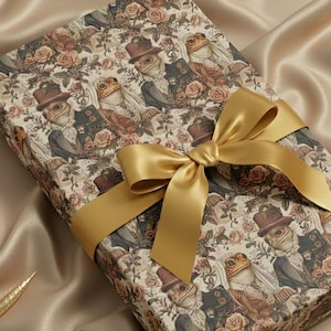 Op de afbeelding: Een cadeauverpakking met een gouden satijnen lint. Het cadeaupapier heeft een patroon van antropomorfe kikkers in pakken en hoeden, omringd door rozen. De achtergrond is een beige satijnen stof met gouden decoraties.