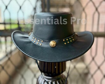 May include: A black leather cowboy hat with a gold band and studs. The hat has a buffalo head design on the front.