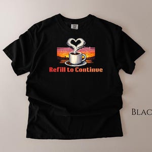 May include: Black t-shirt with a graphic of a coffee cup with steam shaped like a heart, set against a sunset background. The text "Refill to Continue" is below the image. The word "BLACK" is printed on the lower right.