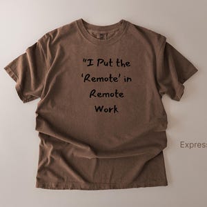May include: Espresso-colored t-shirt with the text "I Put the 'Remote' in Remote Work" in black. The shirt is a crew neck style and has short sleeves. The word "Expresso" is printed on the bottom right.
