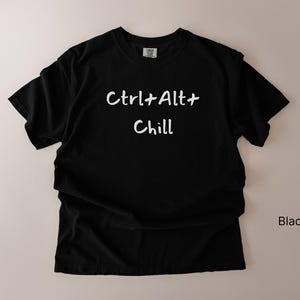 Peut inclure: T-shirt noir avec l'inscription blanche "Ctrl+Alt+Chill", une référence amusante aux raccourcis informatiques. Le t-shirt est de couleur noire unie et semble être fait d'une matière douce.