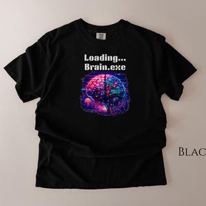May include: Black t-shirt featuring a colorful brain graphic with the text "Loading... Brain.exe". The brain illustration is in shades of pink, blue, and purple, with a futuristic design. The shirt is a casual wear item.