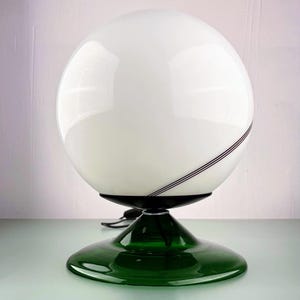 Peut inclure: Lampe de table sphérique blanche avec une base vert foncé. La lampe a une finition brillante et une ligne d'accent noire. La base est de forme circulaire vert foncé. La lampe est de design moderne.
