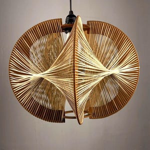 Può includere: Una moderna lampada a sospensione dal design unico. La lampada presenta un motivo intrecciato di spago o cordoncino di colore chiaro, creando una forma geometrica aperta. L'apparecchio è sospeso a un cavo nero.