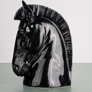 Könnte beinhalten: Eine schwarze Keramik-Pferdekopfskulptur mit glänzender Oberfläche. Die Skulptur ist mit einer Mähne und einer strukturierten Oberfläche detailliert.