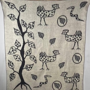 May include: A light grey blanket featuring a black and white pattern. The design includes a tree, birds, leaves, and snakes. The blanket is rectangular with a black border.