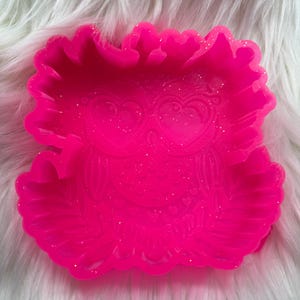 May include: Pink silicone mold shaped like an owl with glitter embedded in the silicone. The owl has large eyes and a heart-shaped design.
