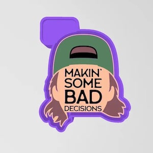 Op de afbeelding: Een paars en groen cartoonfiguur met bruin haar dat een groene hoed draagt met de tekst "Makin' Some Bad Decisions".
