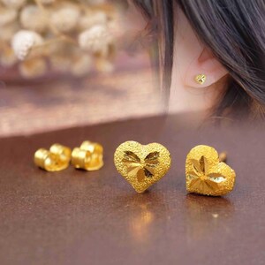 May include: A pair of gold heart-shaped earrings with a textured surface. The earrings are small and delicate.