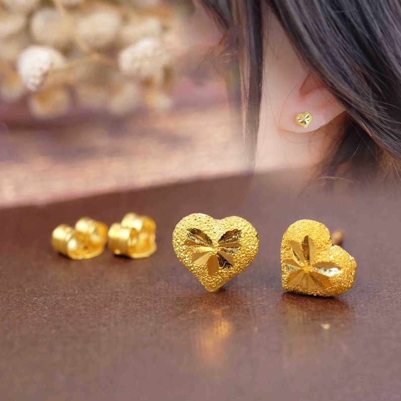 May include: A pair of gold heart-shaped earrings with a textured surface. The earrings are small and delicate.