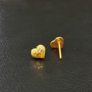 May include: A pair of gold heart-shaped stud earrings. The earrings have a textured surface and are a classic style.