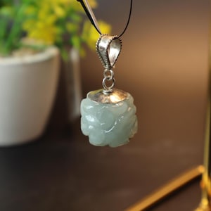 May include: A jade pendant with a silver bail. The jade is carved into a flower shape and is a light green colour.