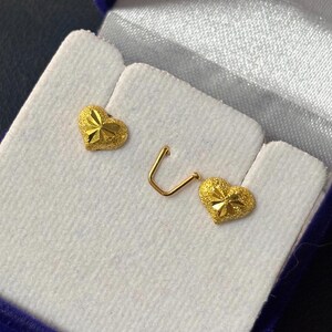 May include: Two gold heart-shaped earrings with a textured surface. The earrings are displayed in a blue velvet box.