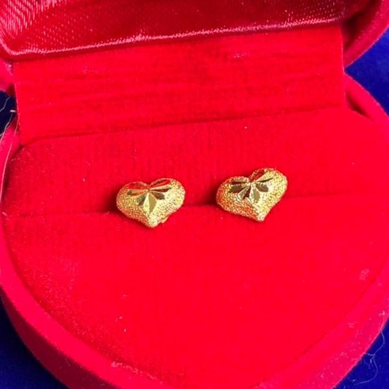May include: A pair of gold heart-shaped earrings with a textured surface, displayed in a red velvet jewelry box.
