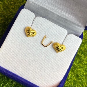 May include: A pair of gold heart-shaped earrings in a white box with a blue velvet lining. The earrings have a textured surface.