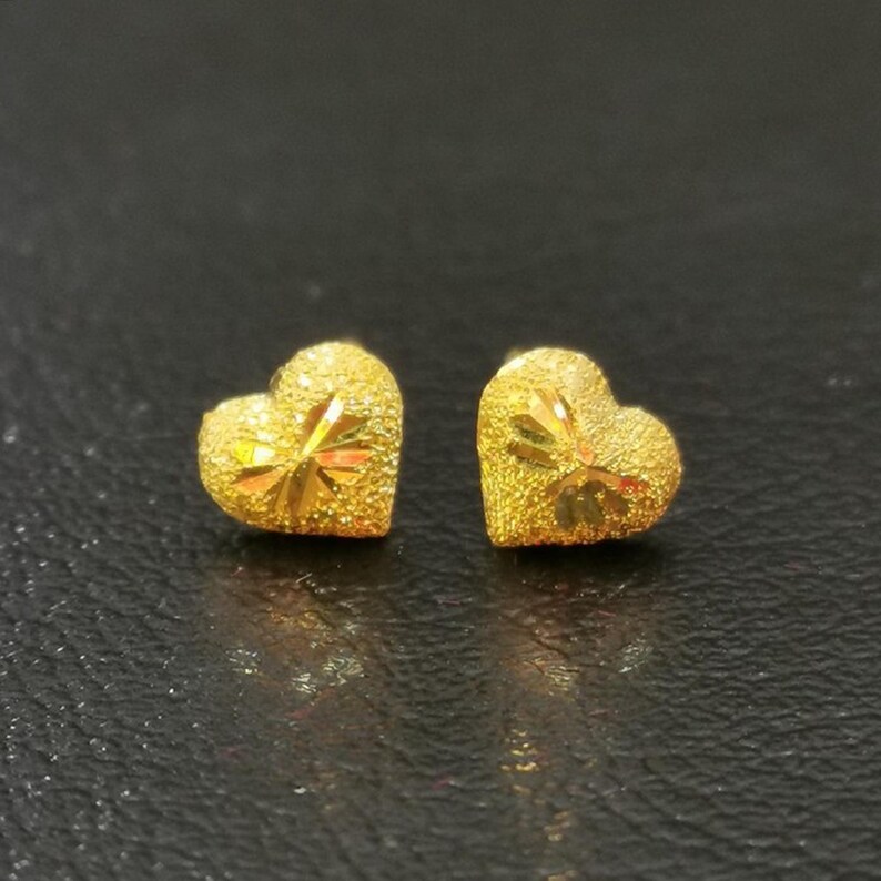 May include: A pair of gold heart-shaped stud earrings. The earrings have a textured surface.