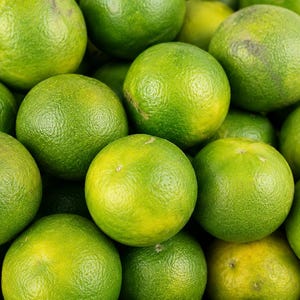May include: A collection of fresh, round citrus fruits with textured, vibrant green and yellow rinds. The fruits are clustered together, displaying varying shades of lime green and pale yellow, with a bumpy, porous skin surface visible on each.