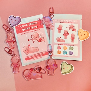 May include: A collection of pink acrylic charms and stickers with a Valentine's Day theme. The set includes keychain charms, heart-shaped stickers, and blind bags with illustrations of cherubs and hearts. The text on the packaging reads "Love Series Blind Bag."