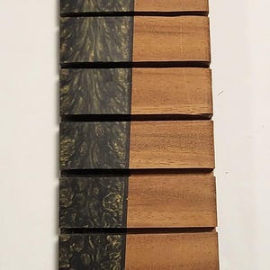 May include: A set of eight rectangular coasters. Each coaster is half dark, swirling resin and half light brown wood. The coasters are arranged vertically against a white background.