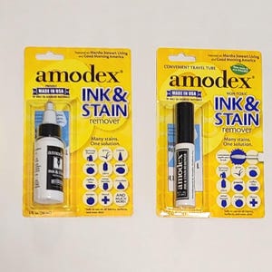 以下が含まれることがあります： 白い表面に、4つのAmodex Ink & Stain Remover製品が表示されています。製品には、箱、ボトル、2つのトラベルチューブが含まれます。パッケージは黄色と青で、ブランド名と製品情報がはっきりと表示されています。