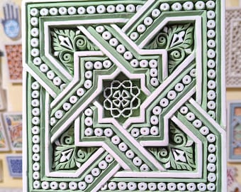 Könnte beinhalten: Eine quadratische, grün-weiße Keramikfliese mit einem komplizierten geometrischen Muster. Die Fliese zeigt eine zentrale Sternform, die von einer Reihe ineinandergreifender Linien und Kreise umgeben ist.