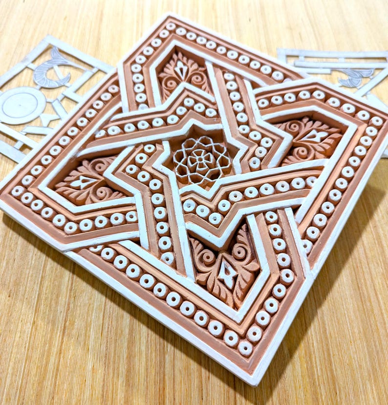 May include: A white and brown ceramic tile with an intricate geometric design. The tile features a star shape with a smaller star in the center. The tile is surrounded by a border of small circles.